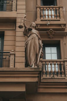 Elegant Justice statue with scales and sword on classic building facade, symbolizing law and fairness.